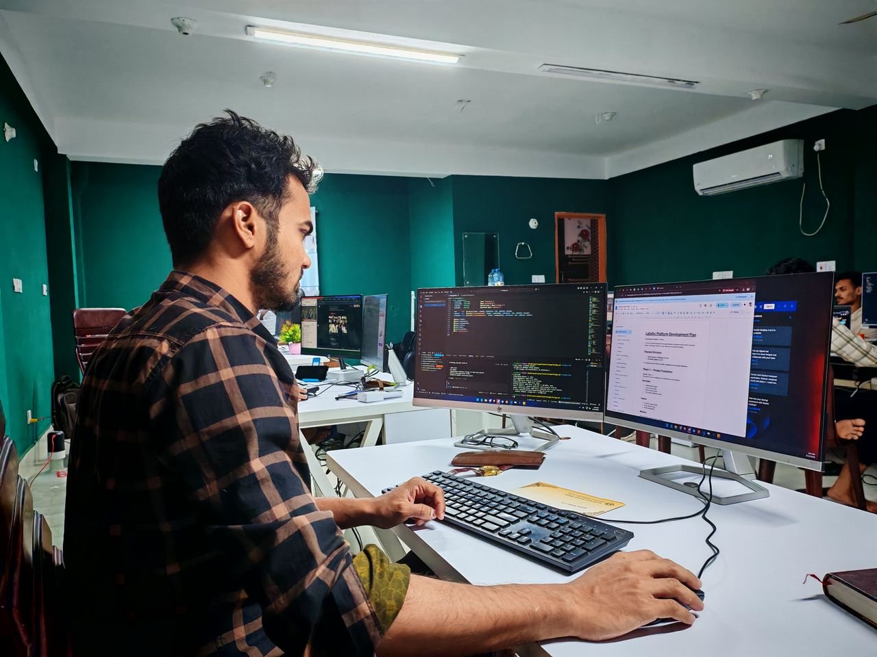 About Software developer coding on dual monitors in a well-lit modern office, focused and engaged.